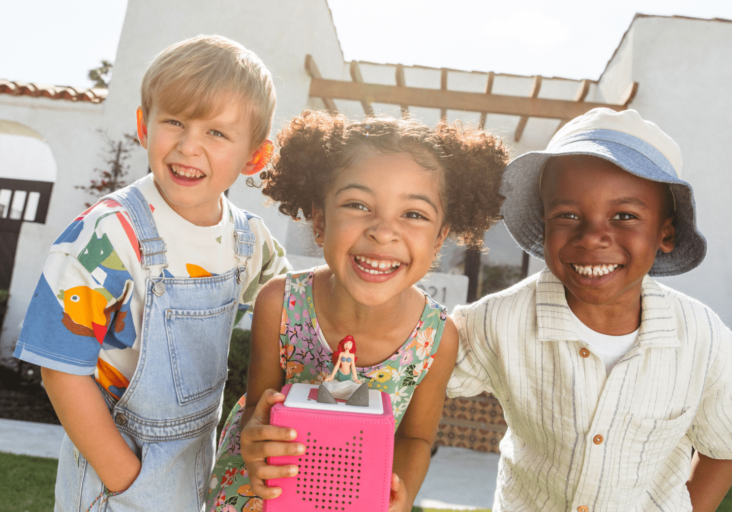 three kids playing and smiling outside with a pink toniebox