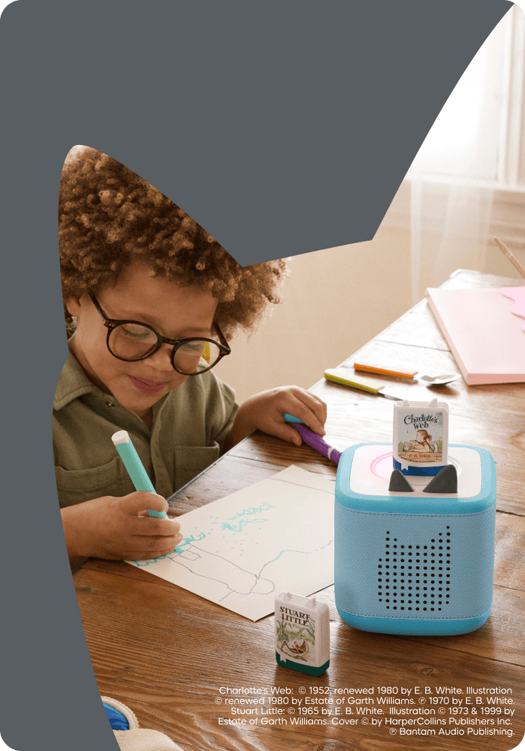 Child with glasses sitting at a desk while listening to Charlotte's Web book Tonie on a blue Toniebox 2