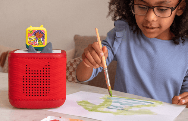 Child painting watercolors while listening to a red Toniebox 2 and Crayola Art Adventures Clever Tonie