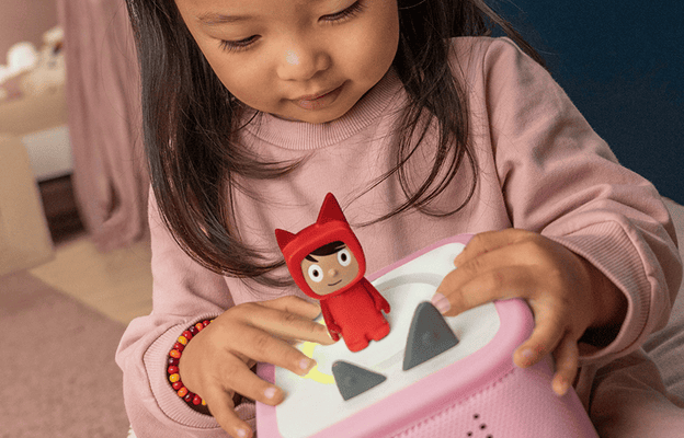 child sitting on the floor holding a pink toniebox 2 while listening to a creative tonie
