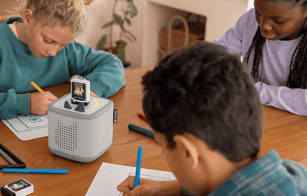 three older children sitting at a table working on homework listening to the Minecraft Book Tonie on a grey Toniebox 2