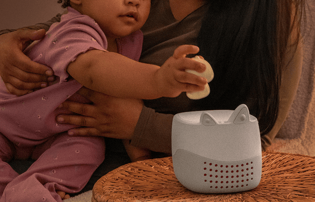 Grey Toniebox Lite on a wicker side table while a young child being held by a parent places the sleepy duck Tonie on top.