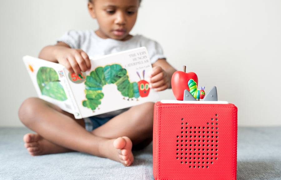 child reading the very hungry caterpillar book with tonie and a red toniebox