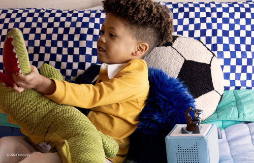 Child playing with stuffed animals and a black panther tonie on a light blue toniebox