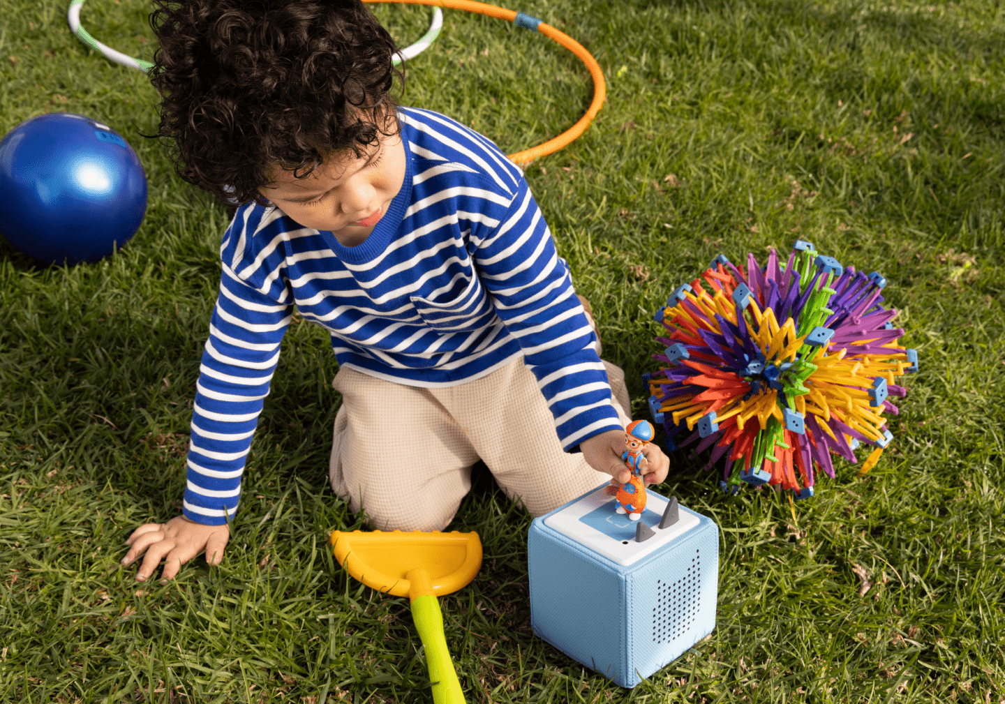 little boy playing outside with blippi tonie and a blue toniebox