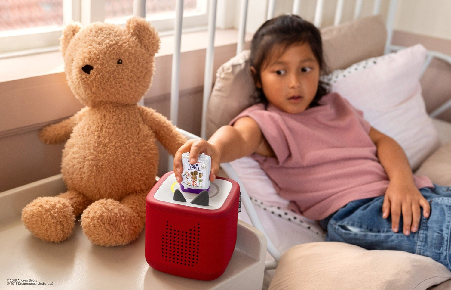 child sitting on a bed listening to Ada Twist audiobooks for kids on a red Toniebox 2