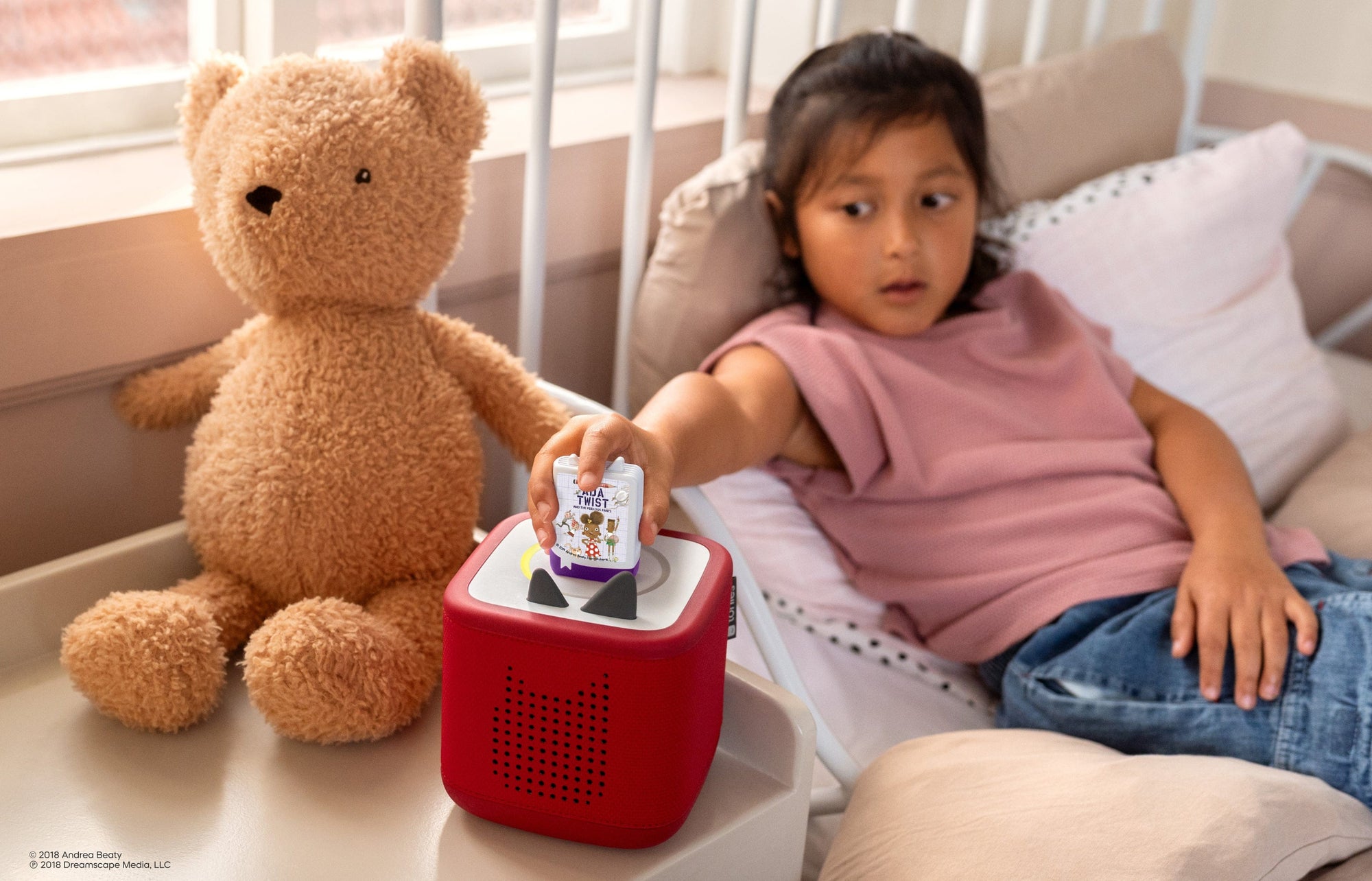 child sitting on a bed listening to Ada Twist audiobooks for kids on a red Toniebox 2
