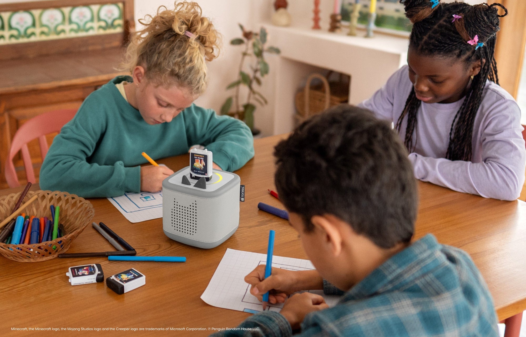 three children coloring while listening to Minecraft audiobooks for kids on a grey Toniebox 2