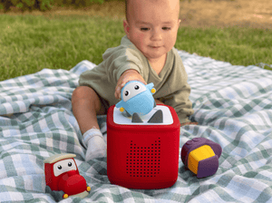 child playing on the ground outside with a toniebox 2 and a my first tonies travel set