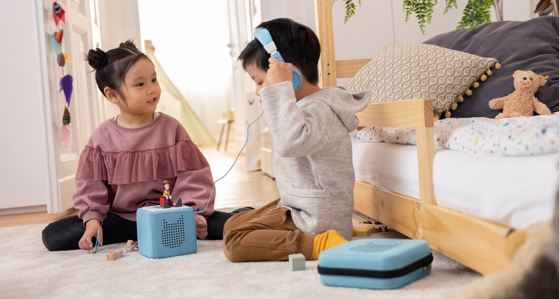 Two children listening to headphones and the blue Toniebox
