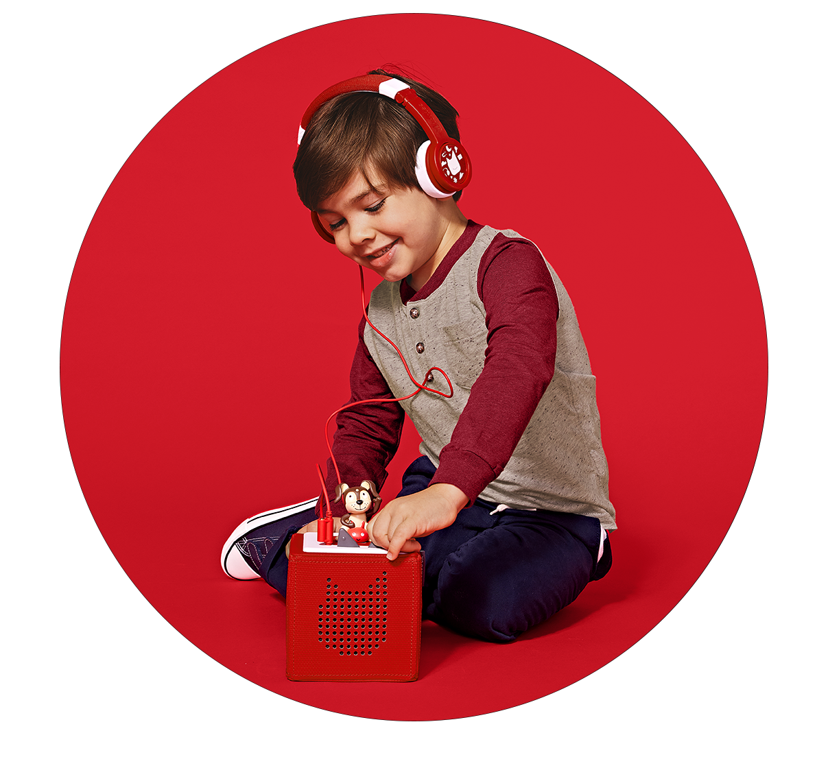 Young boy wearing red tonies headphones and playing with Red Toniebox