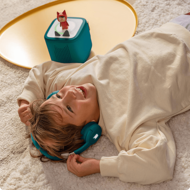 child listening to a Creative-Tonie with a teal Toniebox  and teal bluetooth headphones