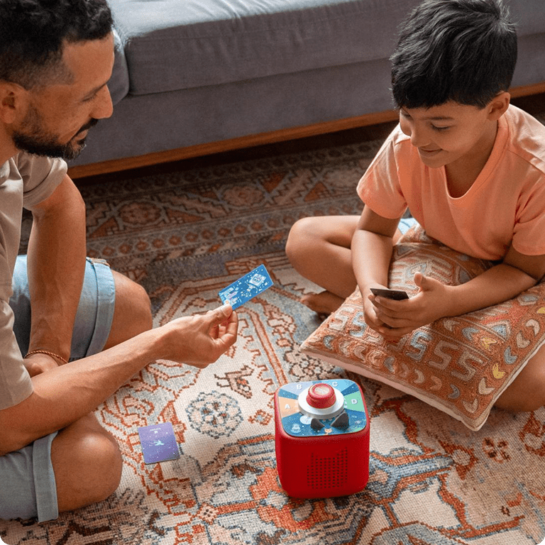 Man and child playing a Tonieplay game with the sunset red Toniebox 2