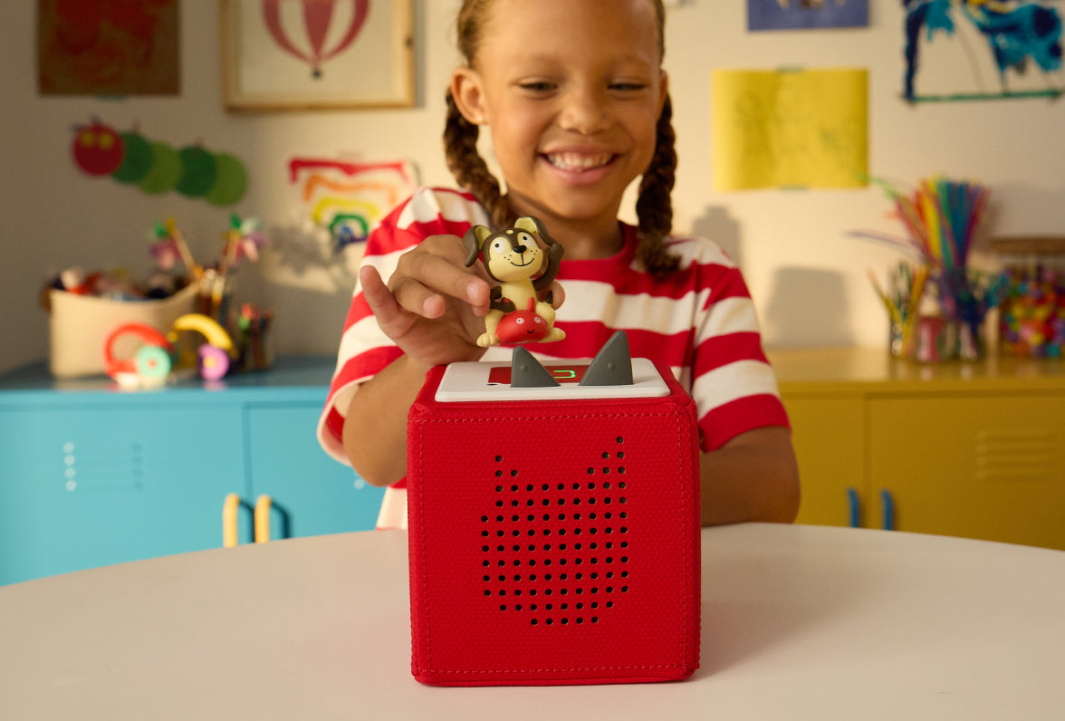 child smiling putting the playtime puppy tonie on a red toniebox