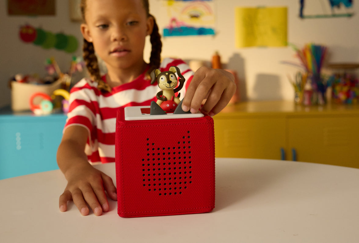 child smiling putting the playtime puppy tonie on a red toniebox